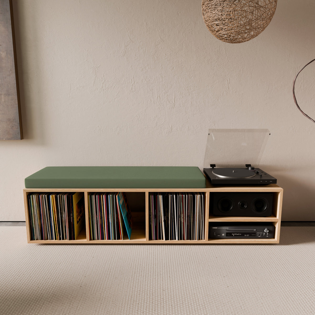 Vue de face d'une banquette de rangement pour vinyles en chêne massif avec un coussin d'assise vert forêt, accueillant une collection de disques, une platine et un amplificateur.