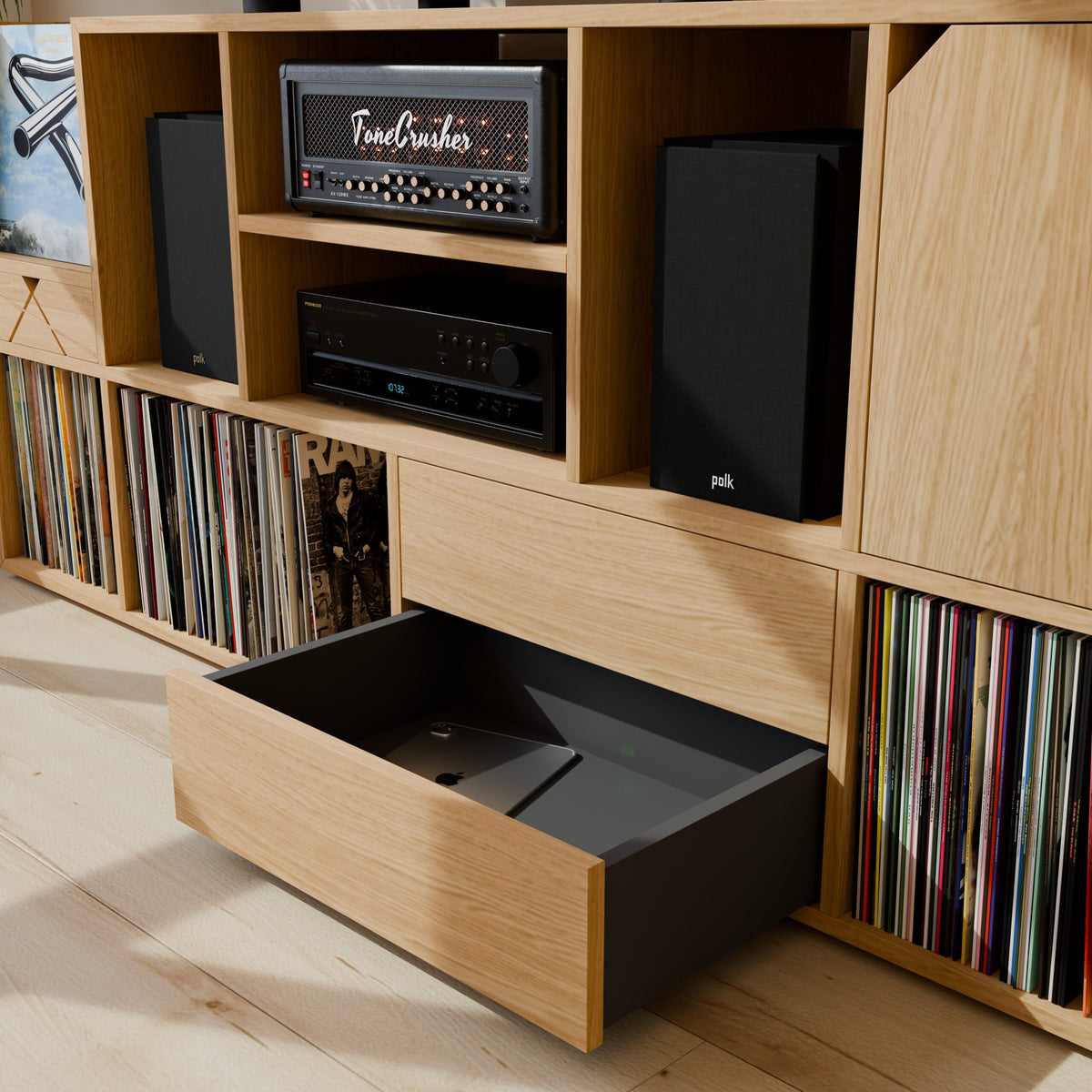 Détail d'un tiroir ouvert sous la station de mixage montrant le rangement d'une tablette, avec vue sur l'amplificateur et les enceintes Polk à proximité.